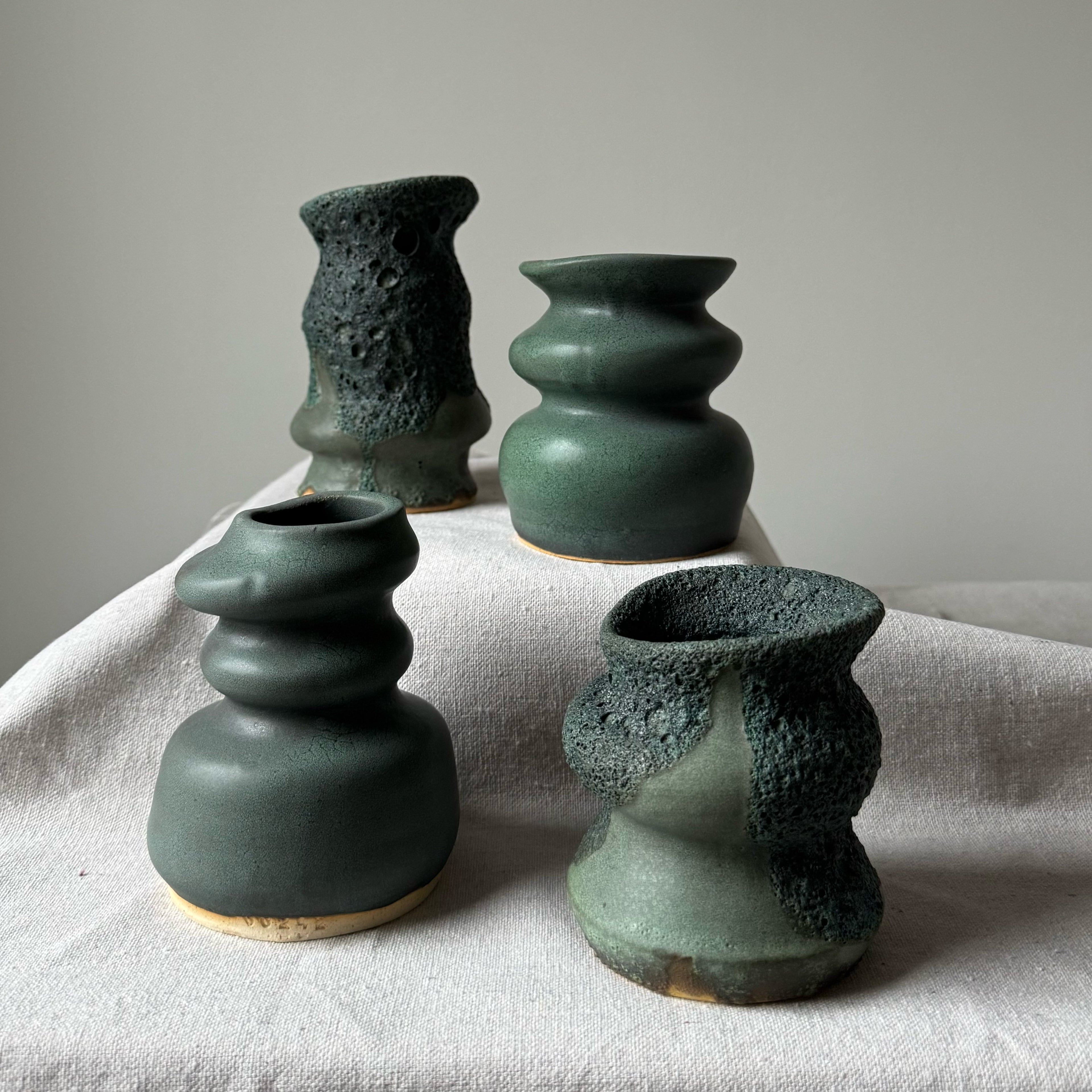 Four green ceramic vases with textured surfaces on a light fabric surface.