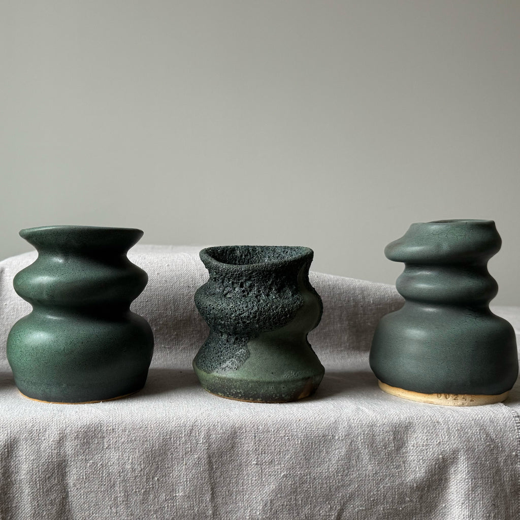 Three green ceramic vases of different shapes on a light fabric surface with a neutral background