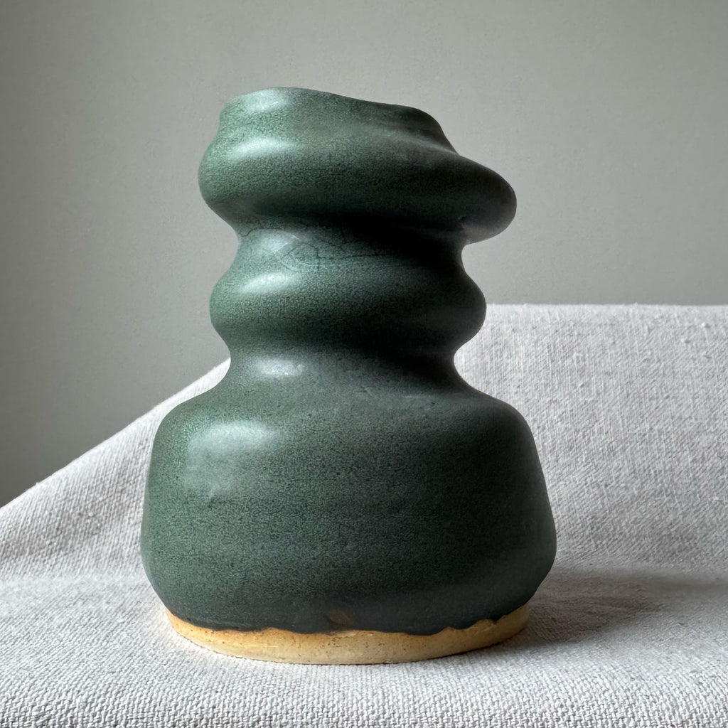 Green ceramic vase on a light gray surface with a neutral background