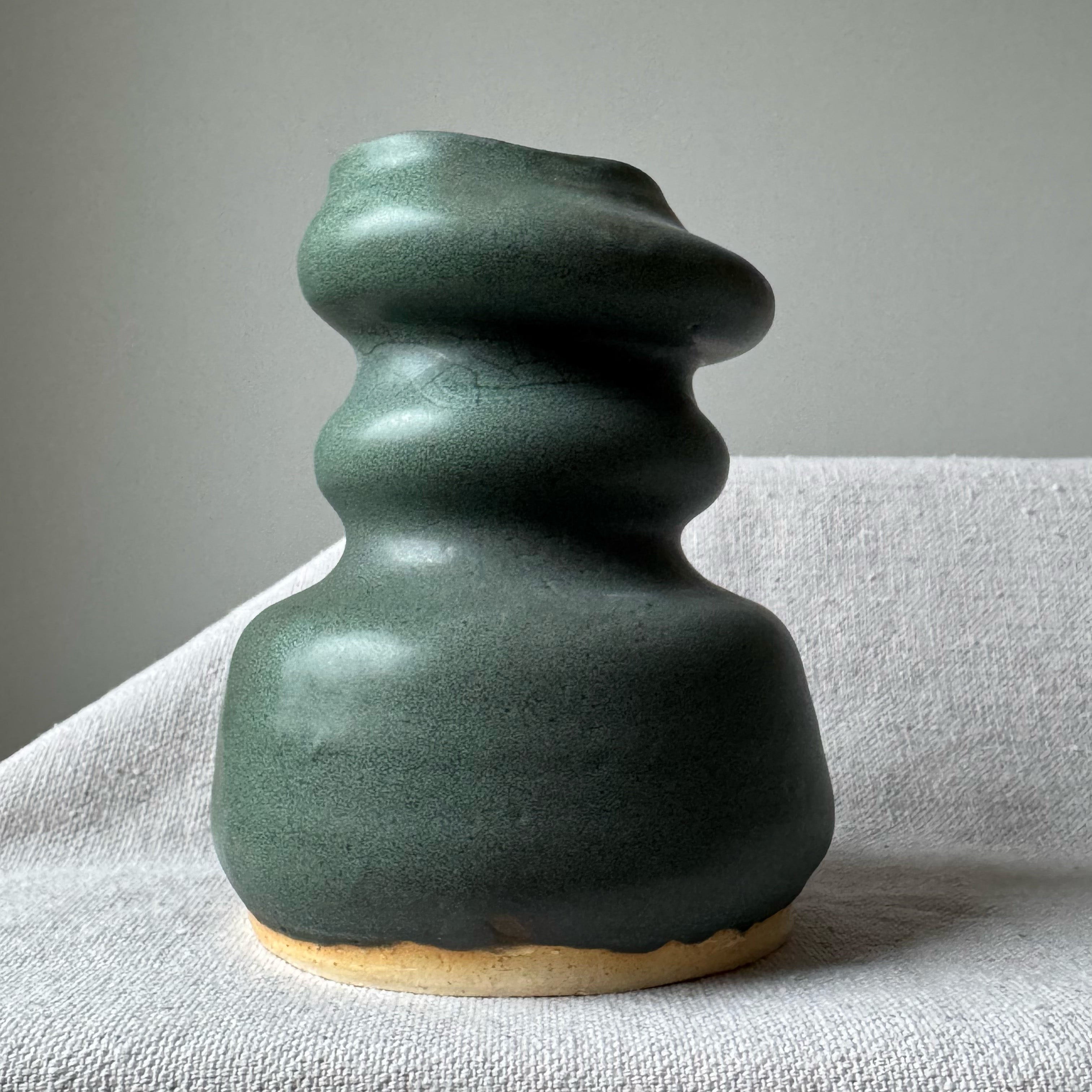 Green ceramic vase on a light gray surface with a neutral background