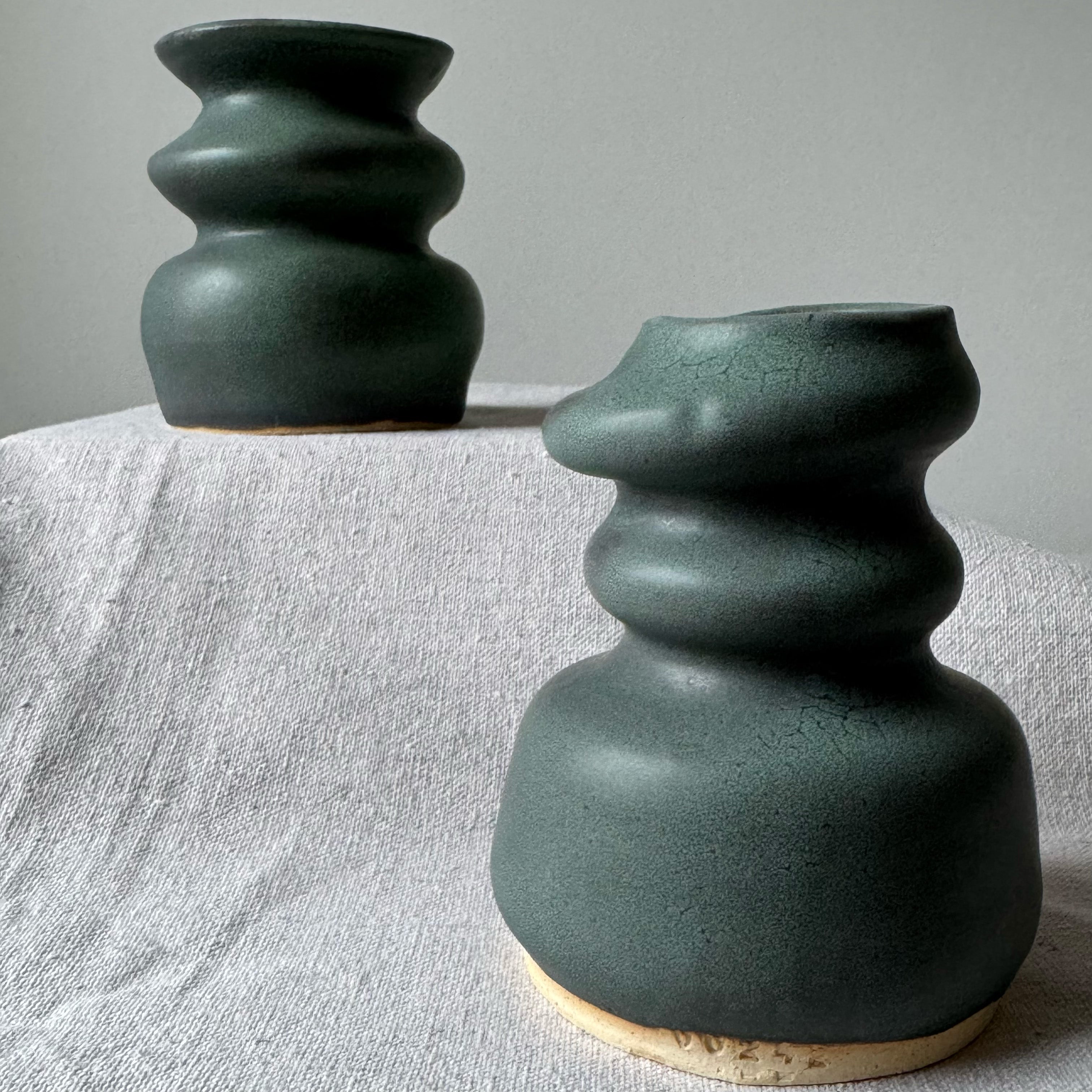 Two green ceramic vases on a textured surface with a neutral background