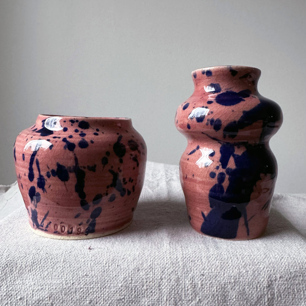 Two ceramic vases with abstract blue patterns on a pink glaze.