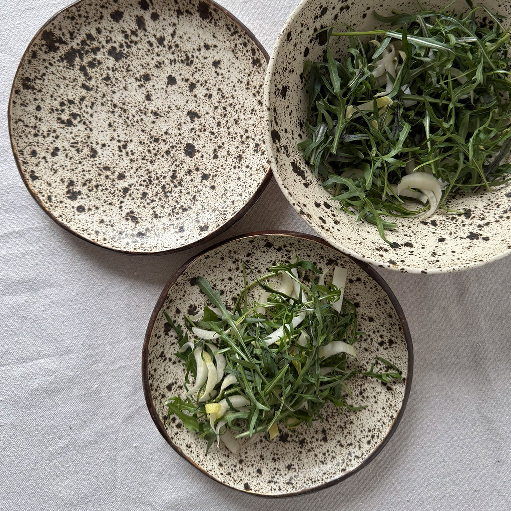 Two speckled ceramic plates and one bowl with green salad on a light gray background