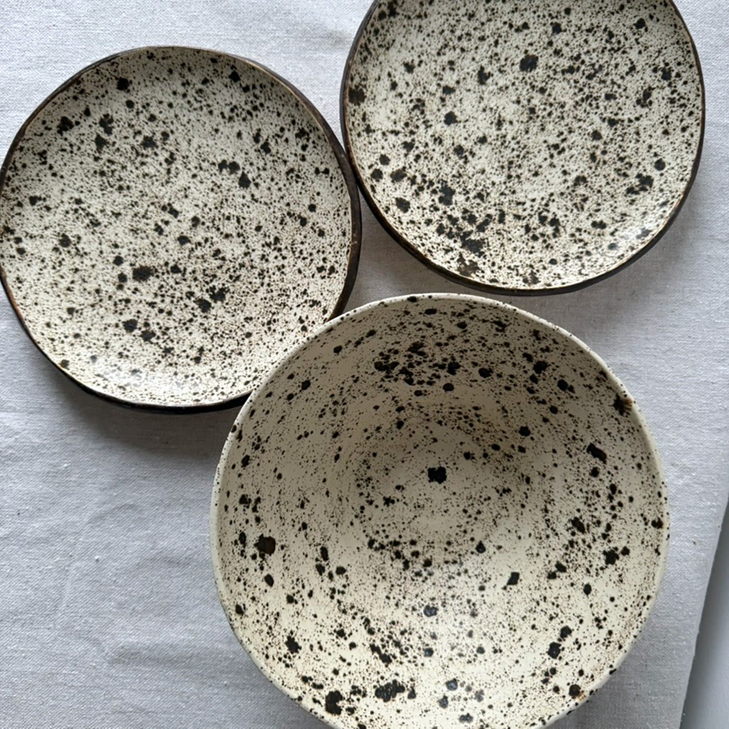 Two ceramic plates and one bowl with speckled pattern on a light gray background