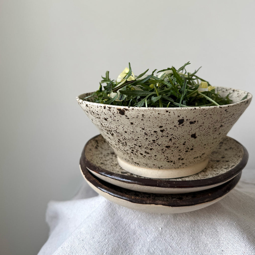 Speckled ceramic bowl with greenery on a white surface