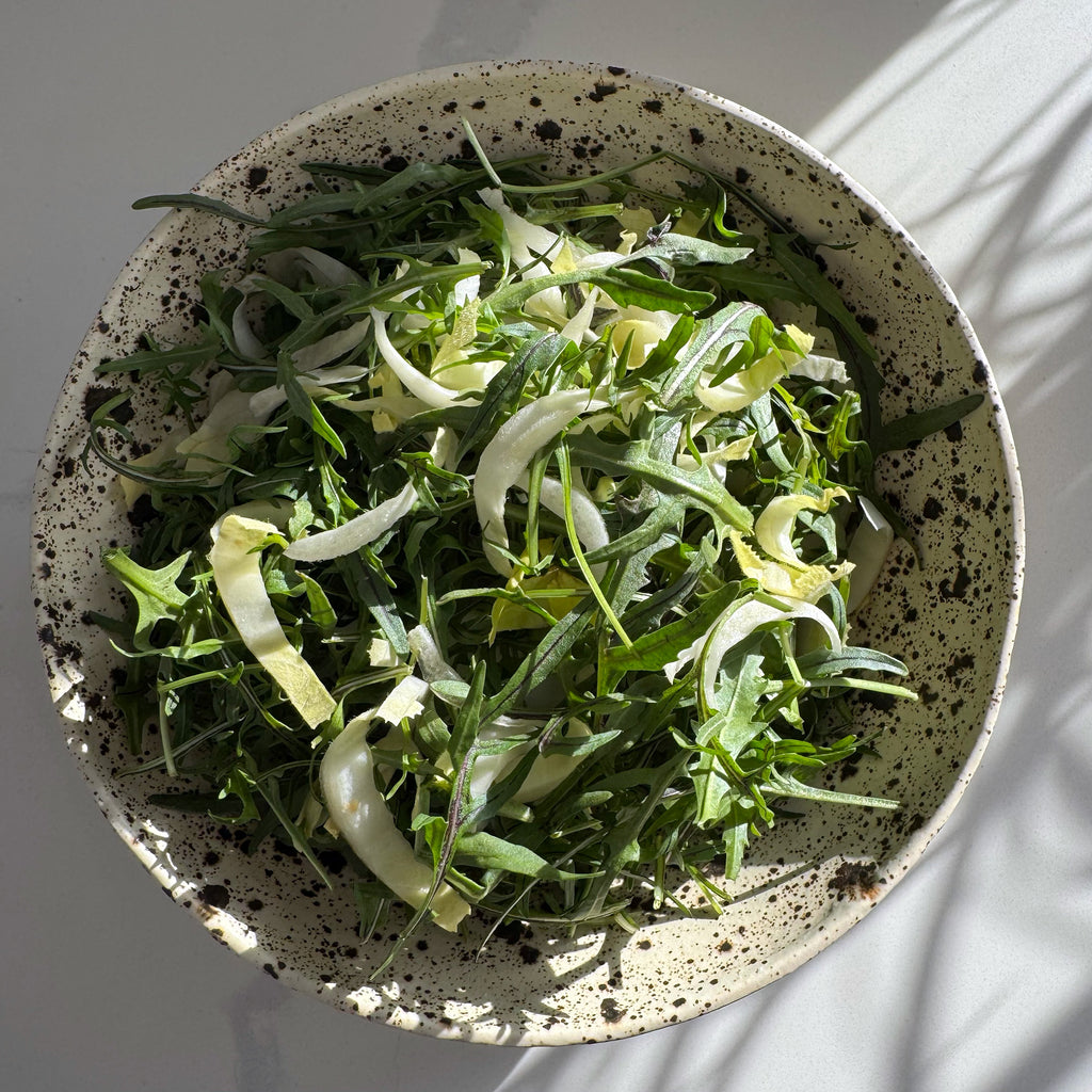 Spotted ceramic bowl filled with green leafy salad on a light background