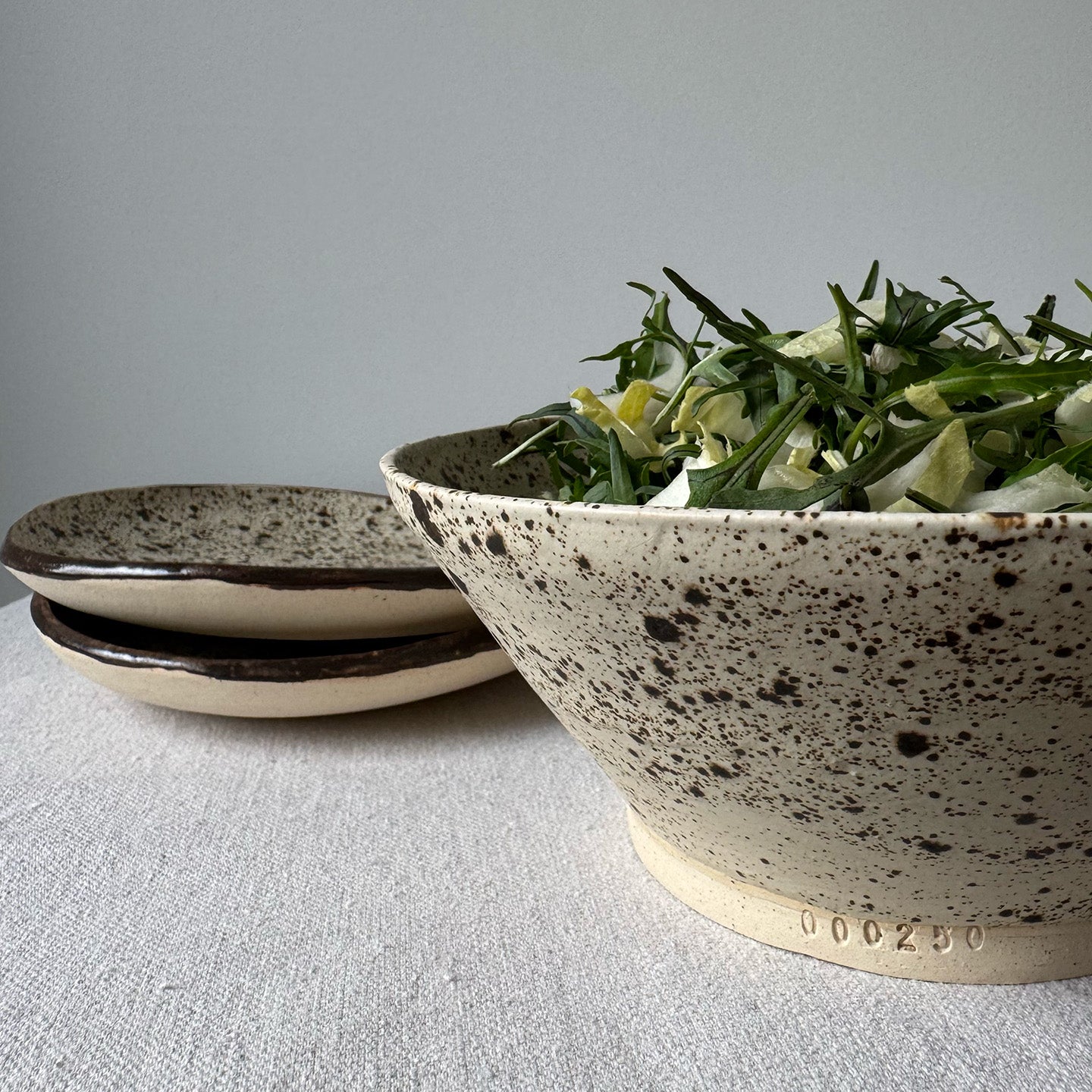 Speckled ceramic bowl with salad on a light gray surface