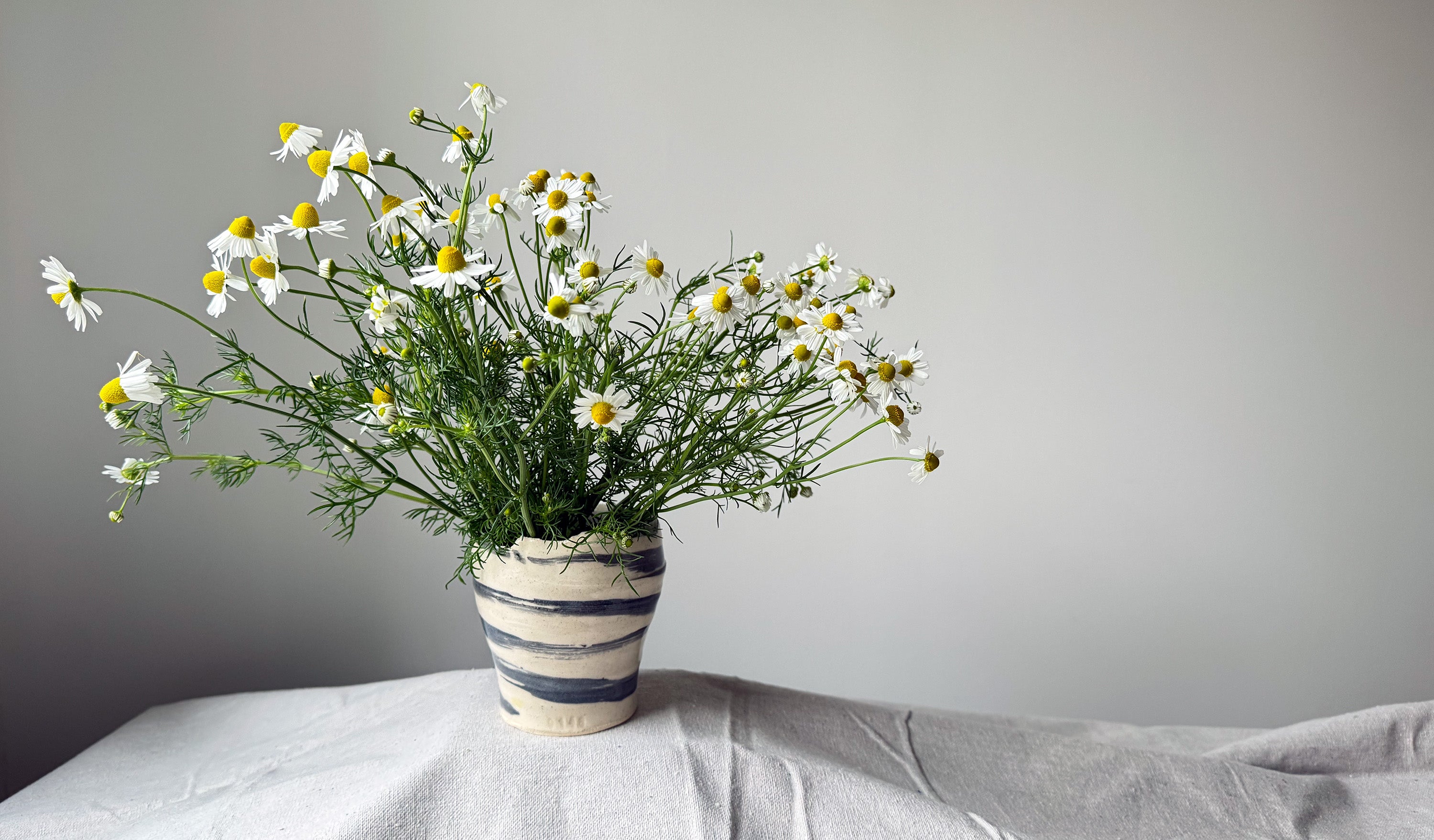 Striped vase with flowers on a light surface against a gray background