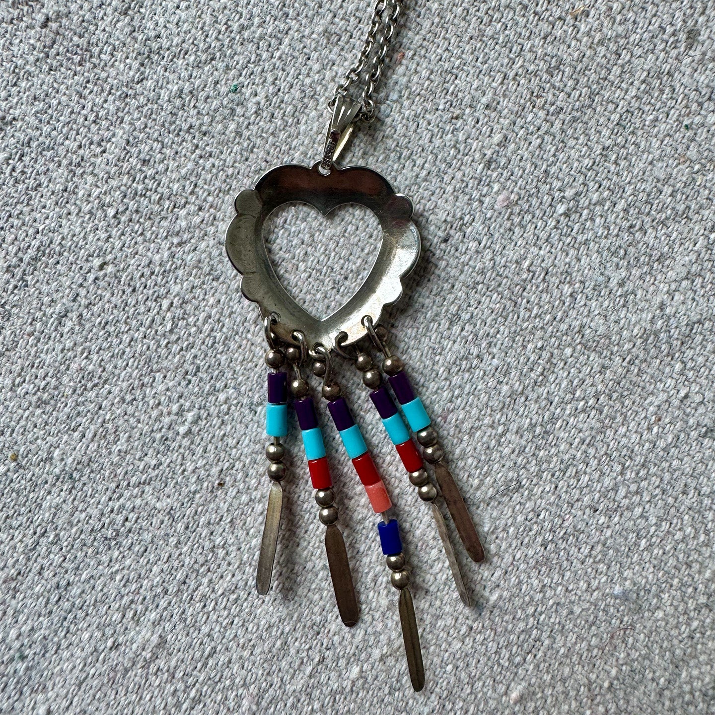 Necklace with heart-shaped pendant and colorful beads on a gray fabric background