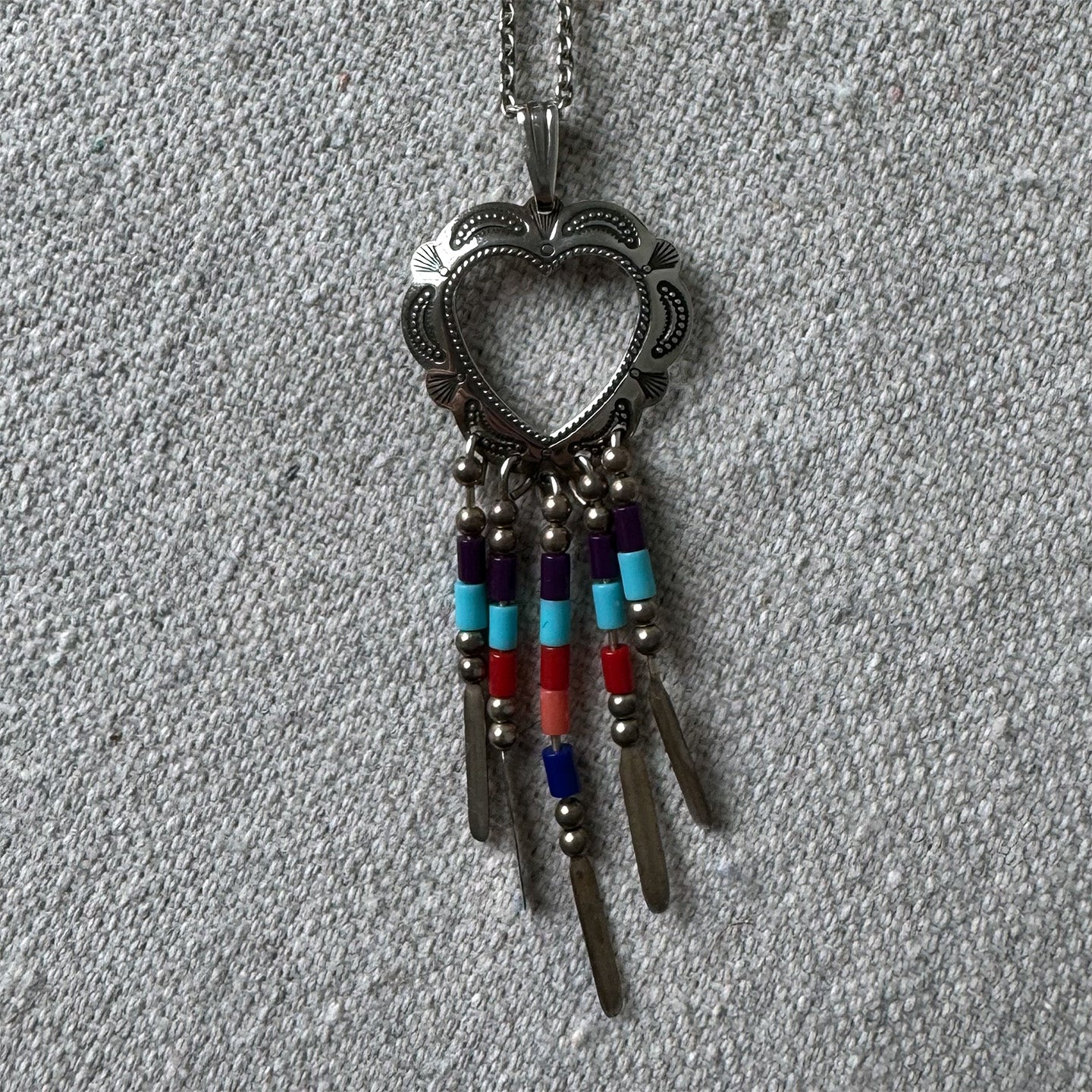 Necklace with heart-shaped pendant and colorful beads on a gray fabric background