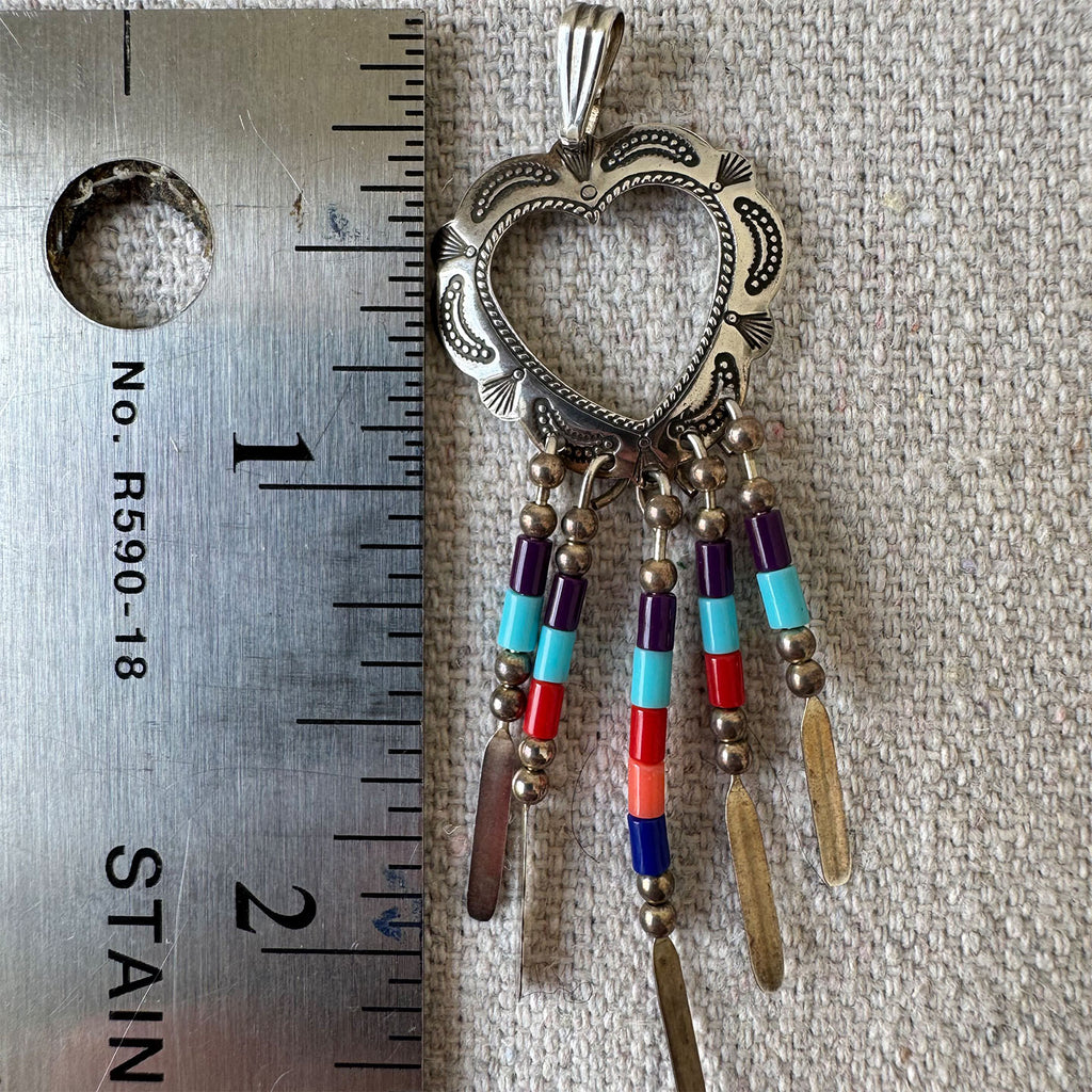 Decorative pendant with colorful beads next to a ruler for scale on a textured surface.