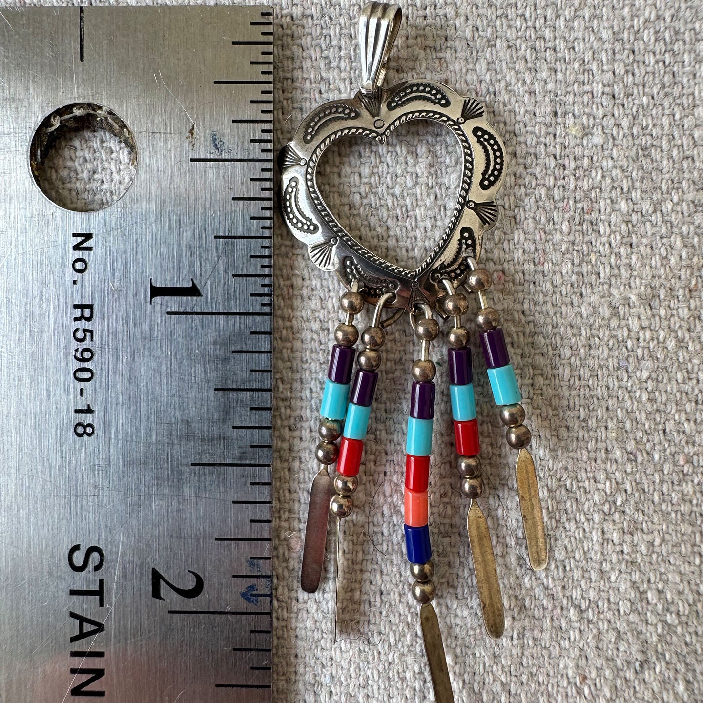 Decorative pendant with colorful beads next to a ruler for scale on a textured surface.