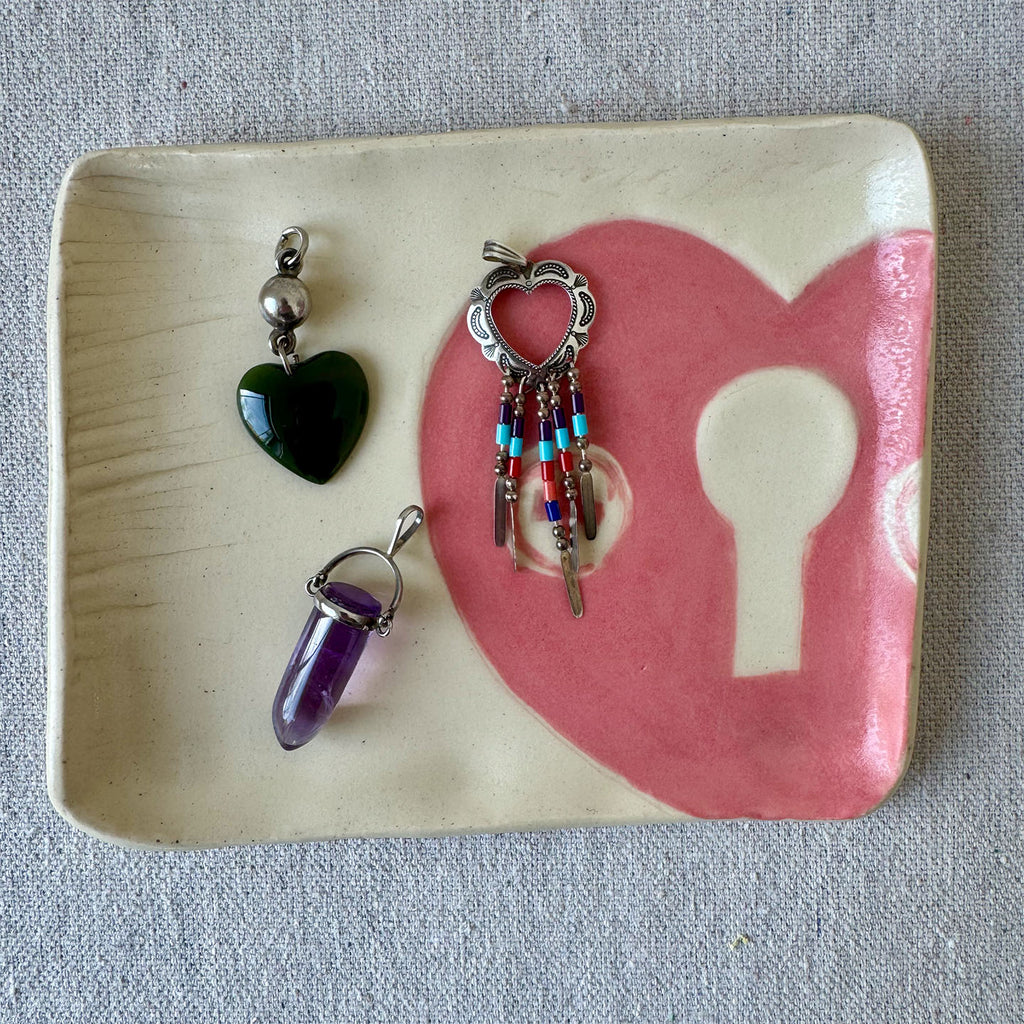 Three jewelry pendants on a ceramic dish with a heart and key design.
