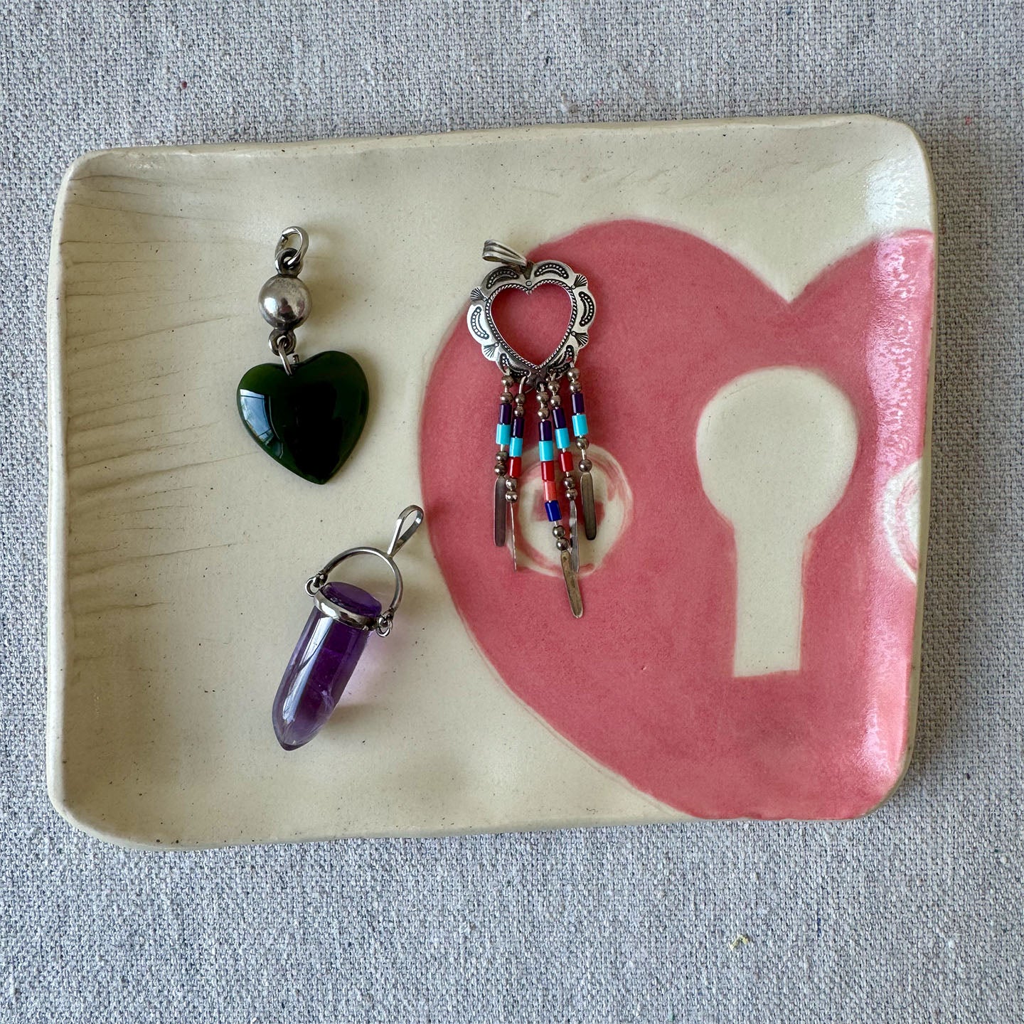Three jewelry pendants on a ceramic dish with a heart and key design.